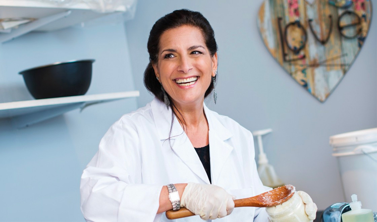 A woman in a lab coat holding a wooden spoon.