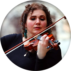 A woman playing a violin in front of a stone wall.