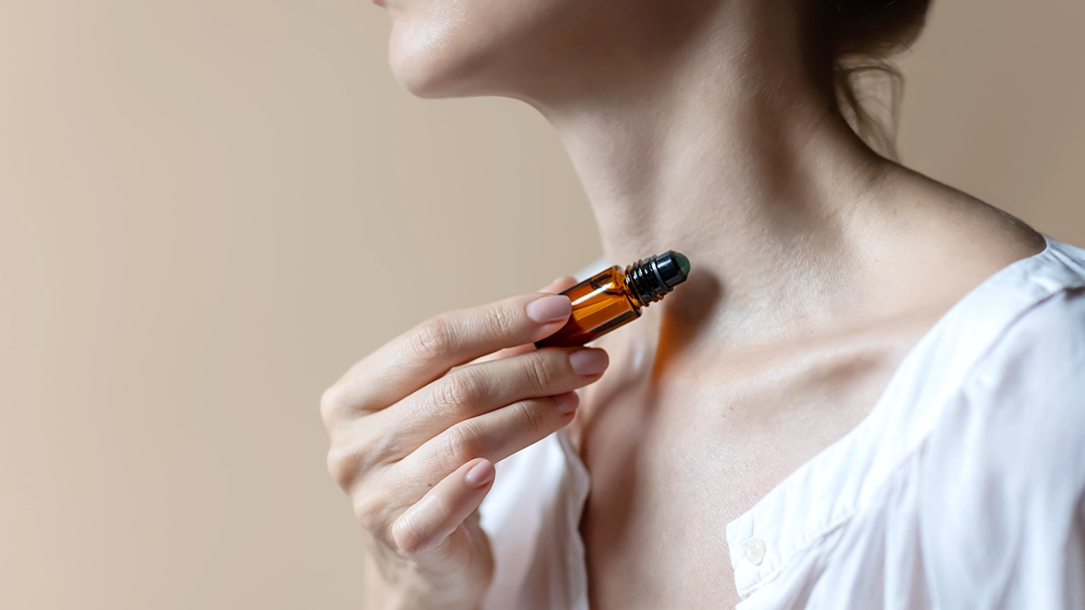 Woman applying Roll-on bottle with essential oil her neck close-up