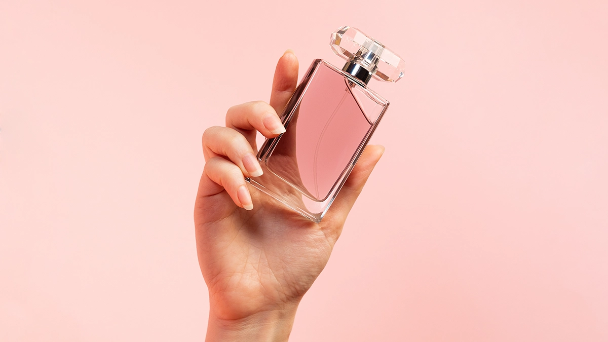 A hand holding a pink perfume bottle, symbolizing fragrance oils made from essential oils and aroma compounds for lasting scents