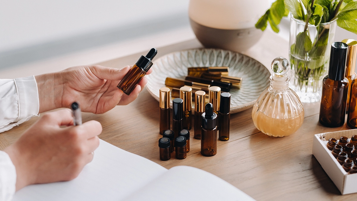 A person holding an amber dropper bottle, surrounded by various amber bottles on a table