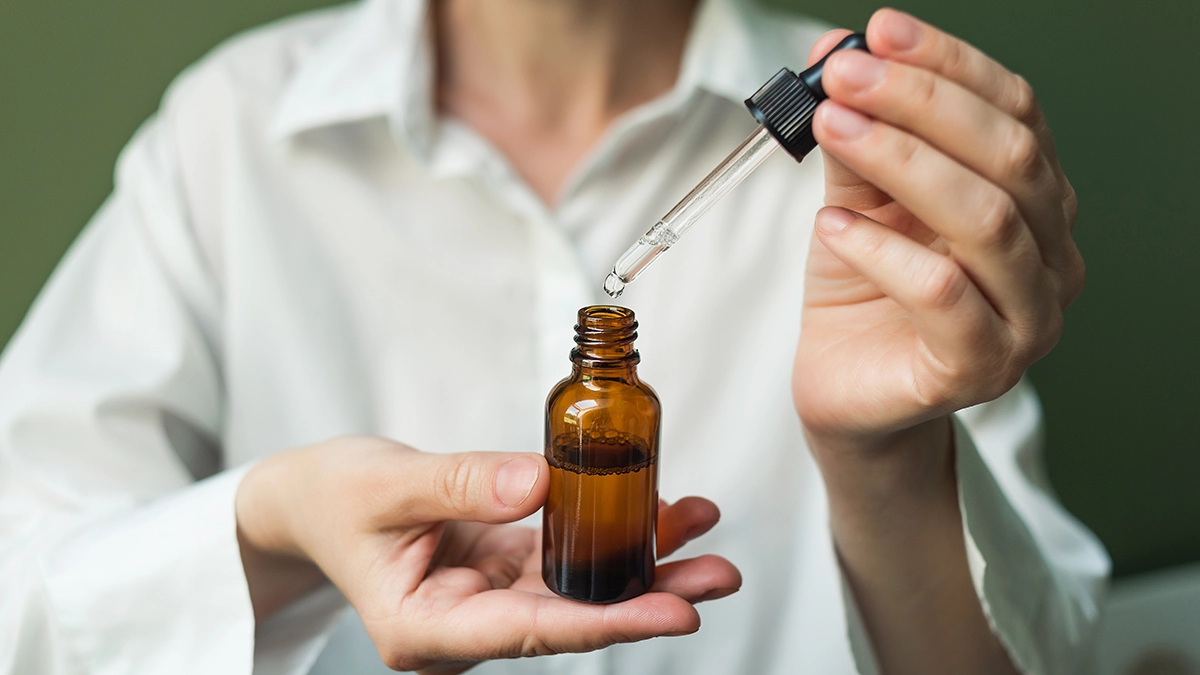 A person uses a dropper to apply essential oil from an amber bottle, showing its use for managing adrenal fatigue