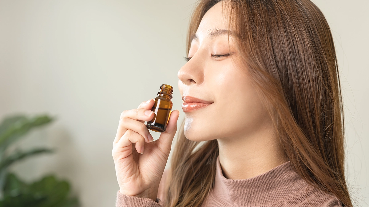 A woman enjoys the scent from a small bottle of essential oil, potentially using it for TMJ (temporomandibular joint) relief