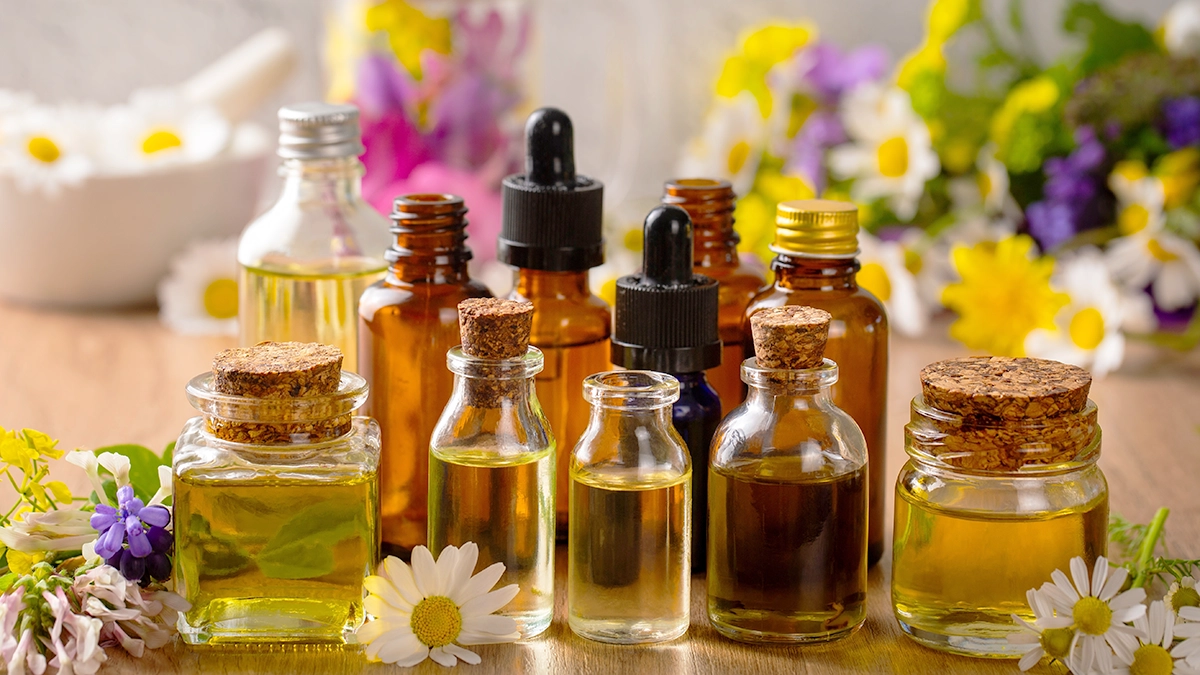 Various bottles of essential oils surrounded by flowers, often used in aromatherapy for TMJ relief