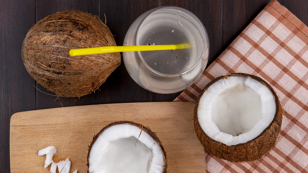 A ripe coconut with pieces of coconut meat on a cutting board, next to a knife and a glass of coconut water Natural Remedies for HFMD