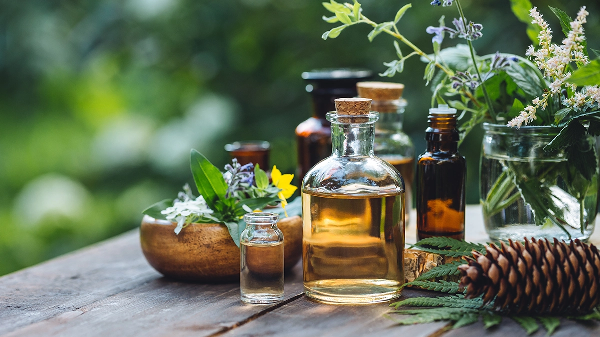 A variety of essential oil bottles and fresh herbs displayed on a wooden table outdoors