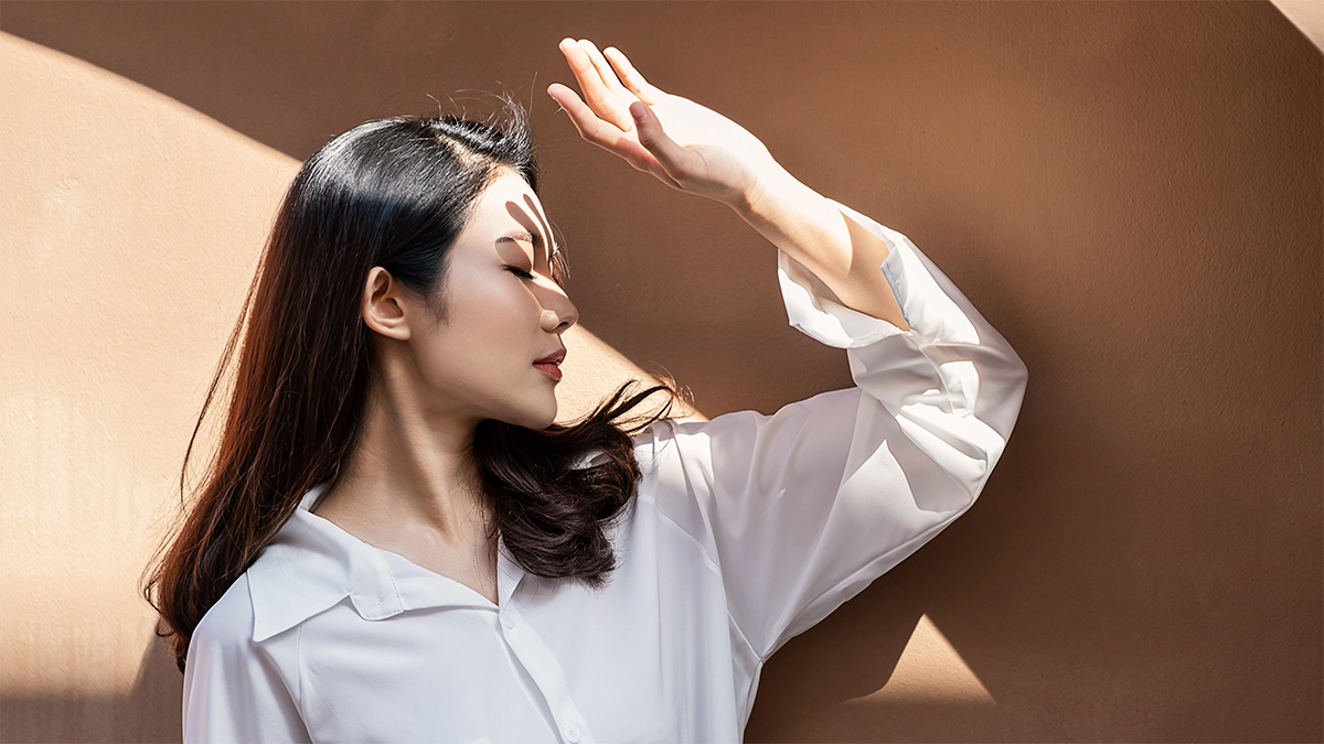 A woman shields her face from sunlight, highlighting the need for protection against UVA and UVB rays