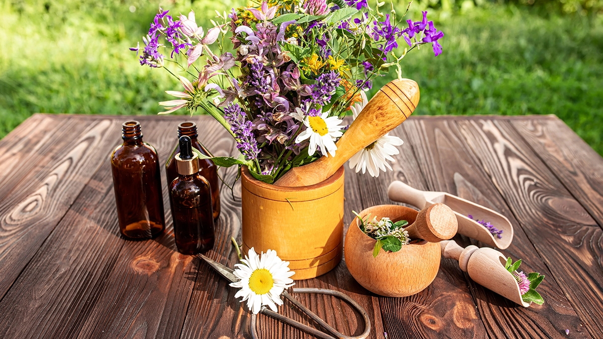 Essential Oils bottles and fresh herbs arranged with a mortar and pestle emphasize the simplicity of DIY natural sunscreen recipes