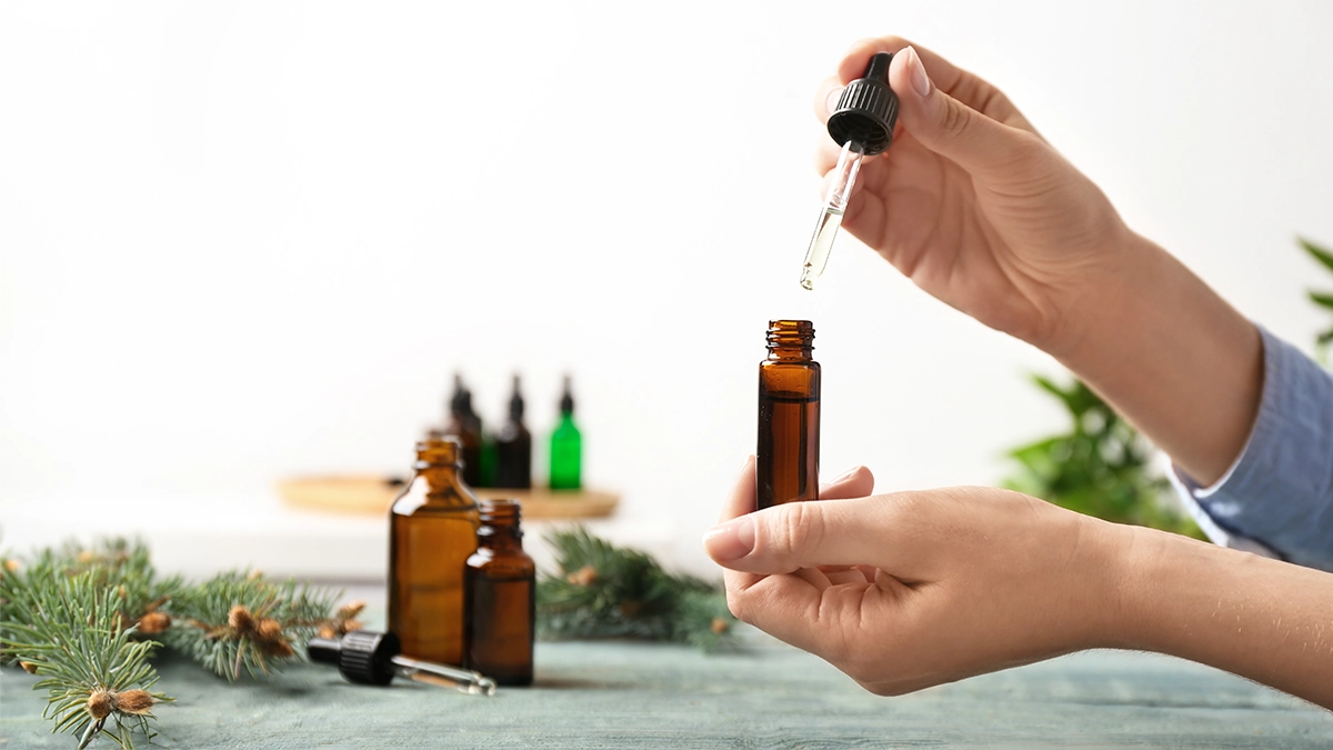 Hands using a dropper to transfer essential oil into an amber bottle, with additional bottles in the background, illustrating safe use for HFMD