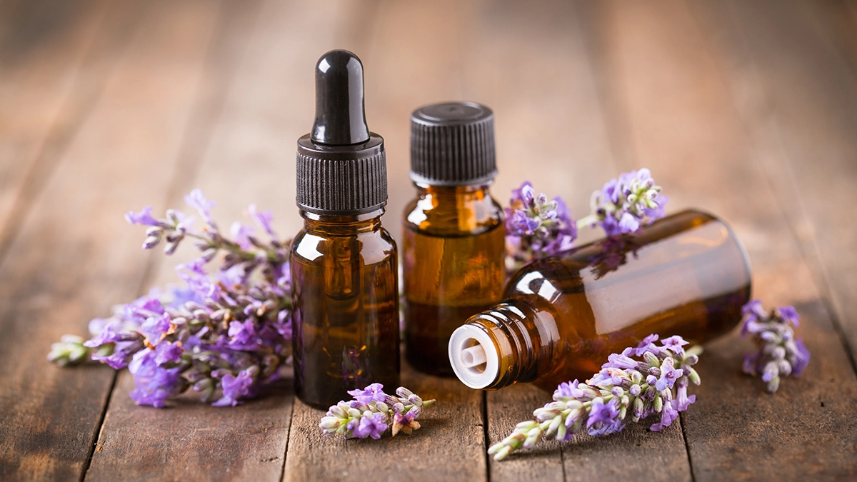 Three amber bottles of essential oils with droppers, surrounded by fresh lavender sprigs, on a rustic wooden surface Essential Oils for Relieving HFMD Symptoms