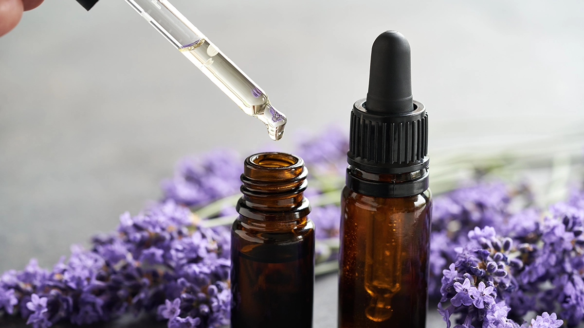 A dropper with essential oil above a bottle, with lavender, showing the soothing benefits of essential oils for skincare