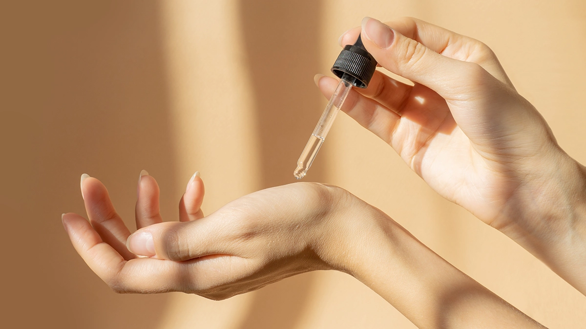  A hand applies essential oil from a dropper onto the palm, showing its use for skin