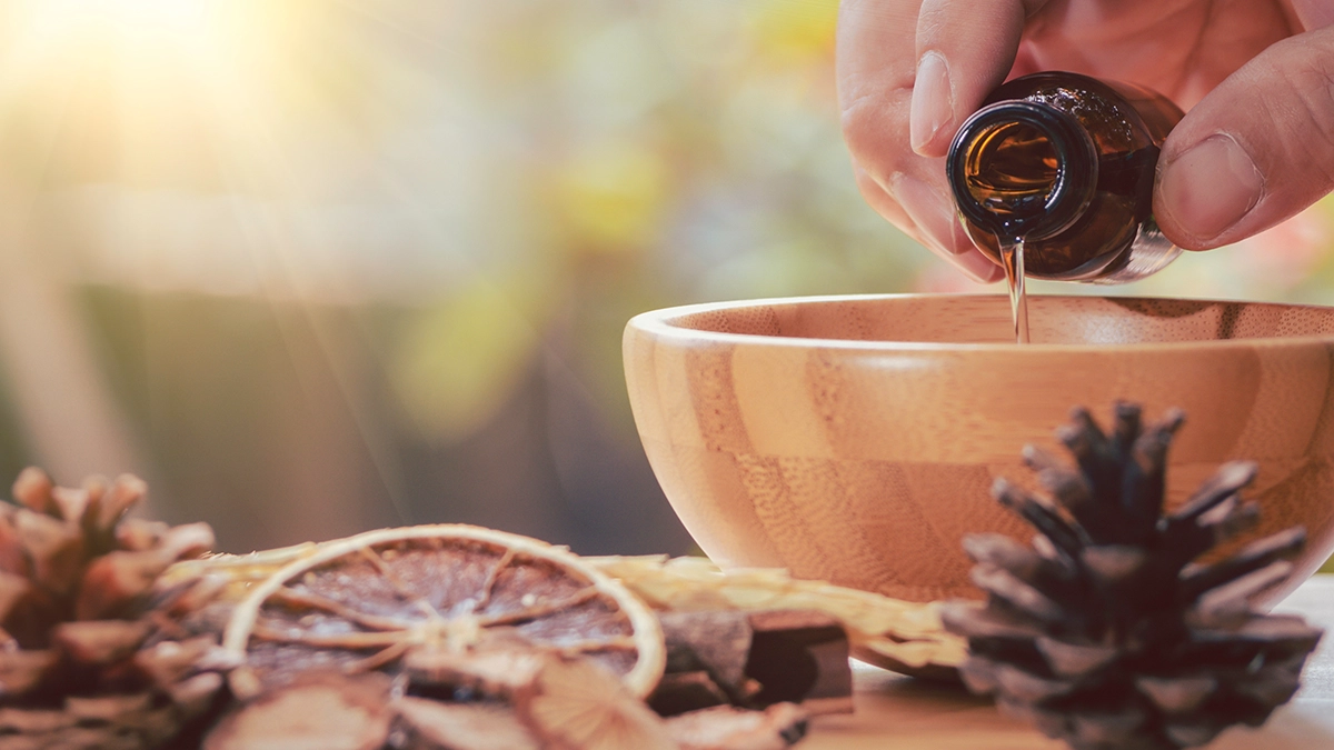 A hand pours essential oil into a wooden bowl surrounded by citrus, representing the creation of a detoxifying massage oil