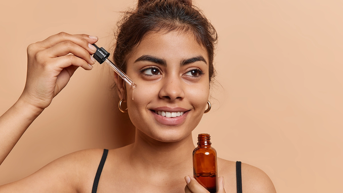 A woman applies essential oil to her face with a dropper, promoting hydration, soothing, and a glowing complexion