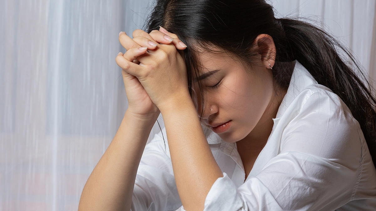 A young woman, hands clasped, expressing the sorrow of grief and its impact on mental health