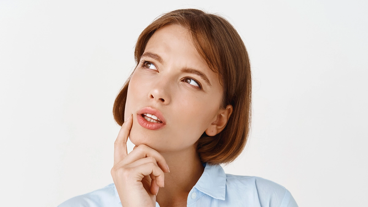 A young woman in a blue blouse thinking, hand on chin, representing understanding detoxification