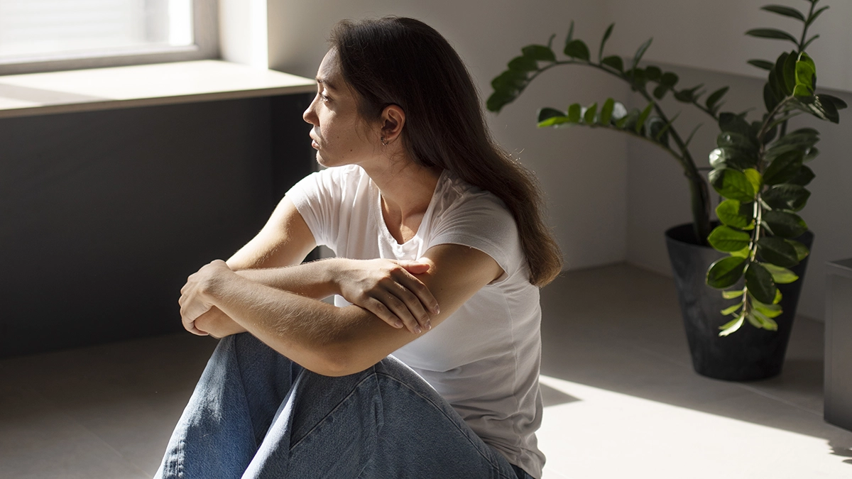 A young woman sits by a window in deep thought, conveying introspection and the isolating nature of OCD symptoms