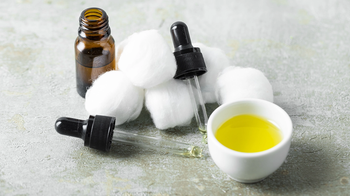 Essential oil dropper, bottle, and cotton balls for safe earache relief; apply diluted oil around, not inside, the ear