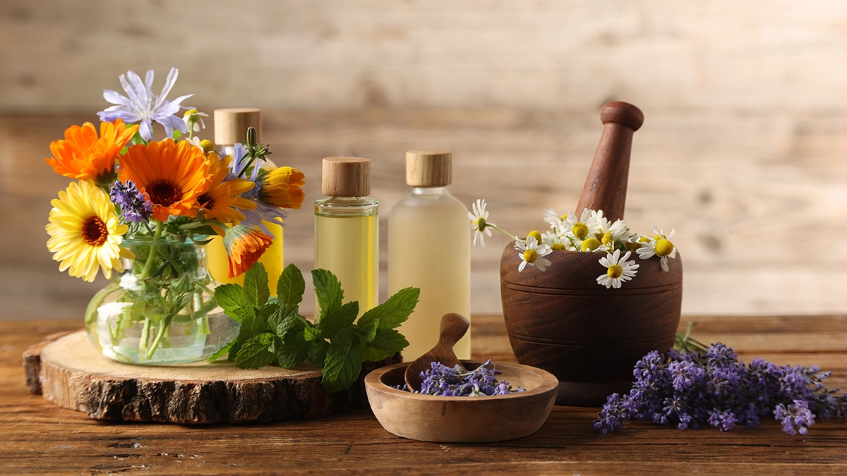 Essential oils, fresh flowers, and herbs on a wooden surface, representing natural remedies for soothing minor burns