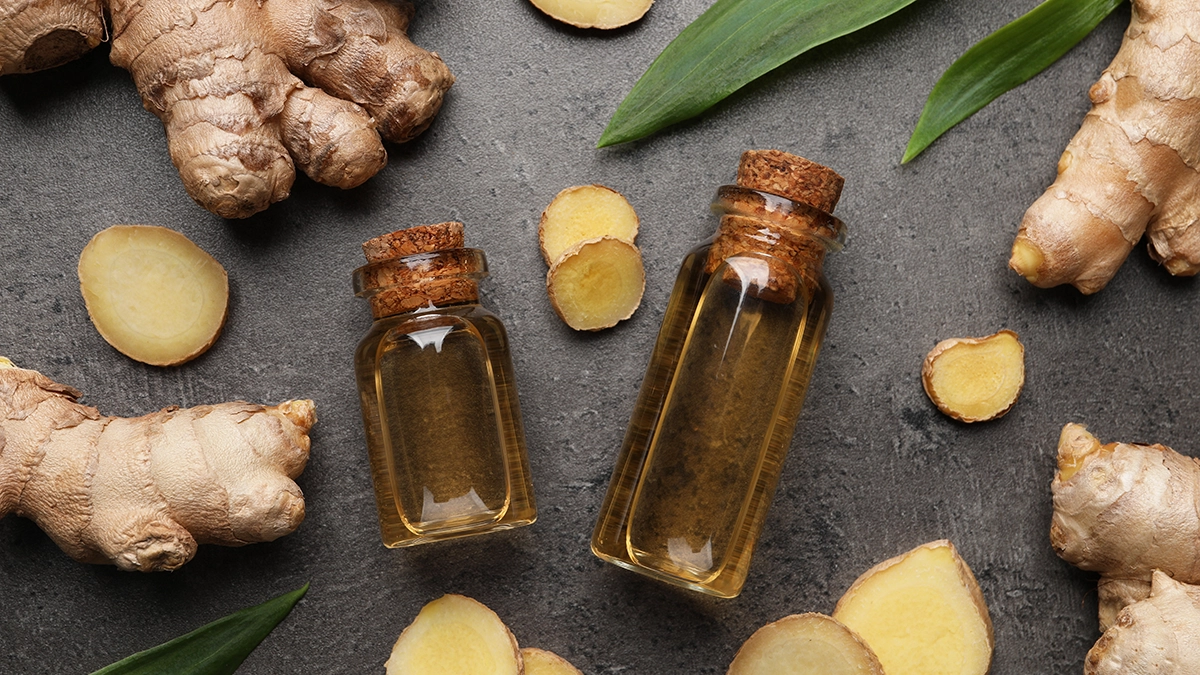 essential oils that are effective for stomach pain relief. Fresh ginger roots and slices arranged around small bottles of essential oil on a gray surface