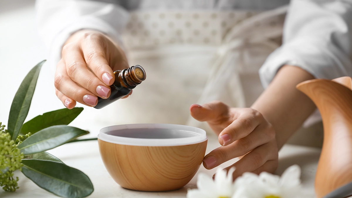 Hands pouring essential oil into a bowl, with leaves and flowers, symbolizing a burn relief blend with lavender and chamomile