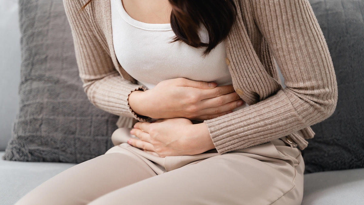 various causes of stomach pain, including digestive problems and cramps. Person holding their abdomen, appearing to experience stomach pain, while sitting on a couch