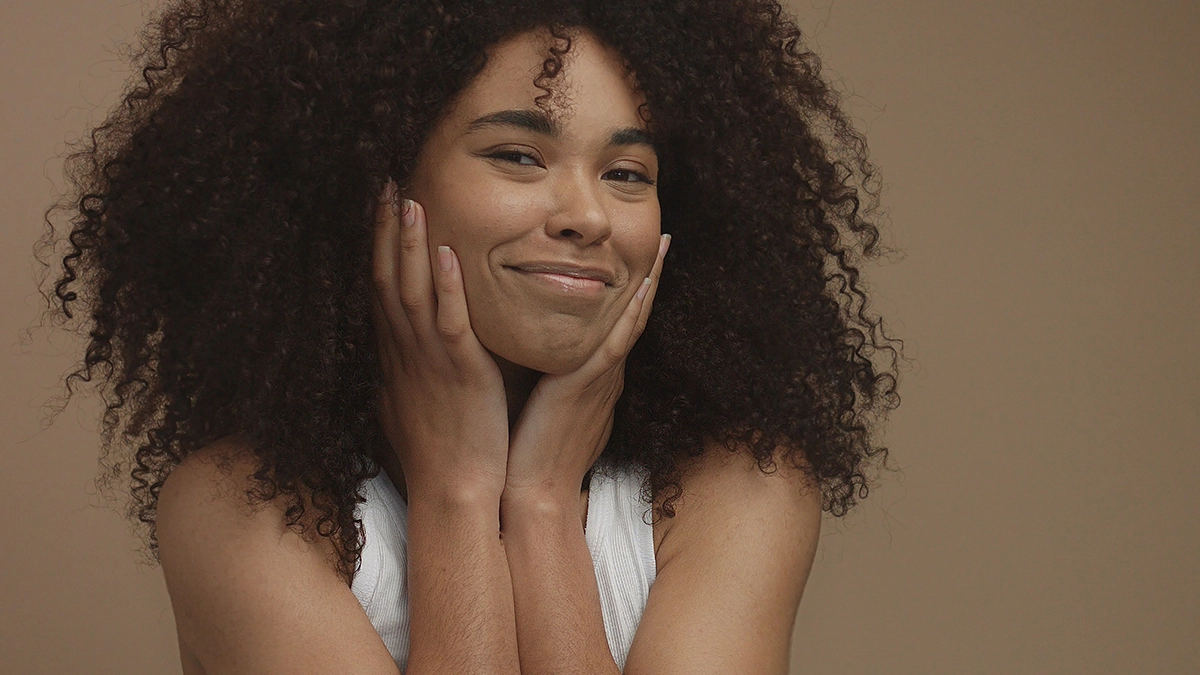 Smiling woman with curly hair touching her face, showing the moisturizing benefits of carrier oils for healthy skin