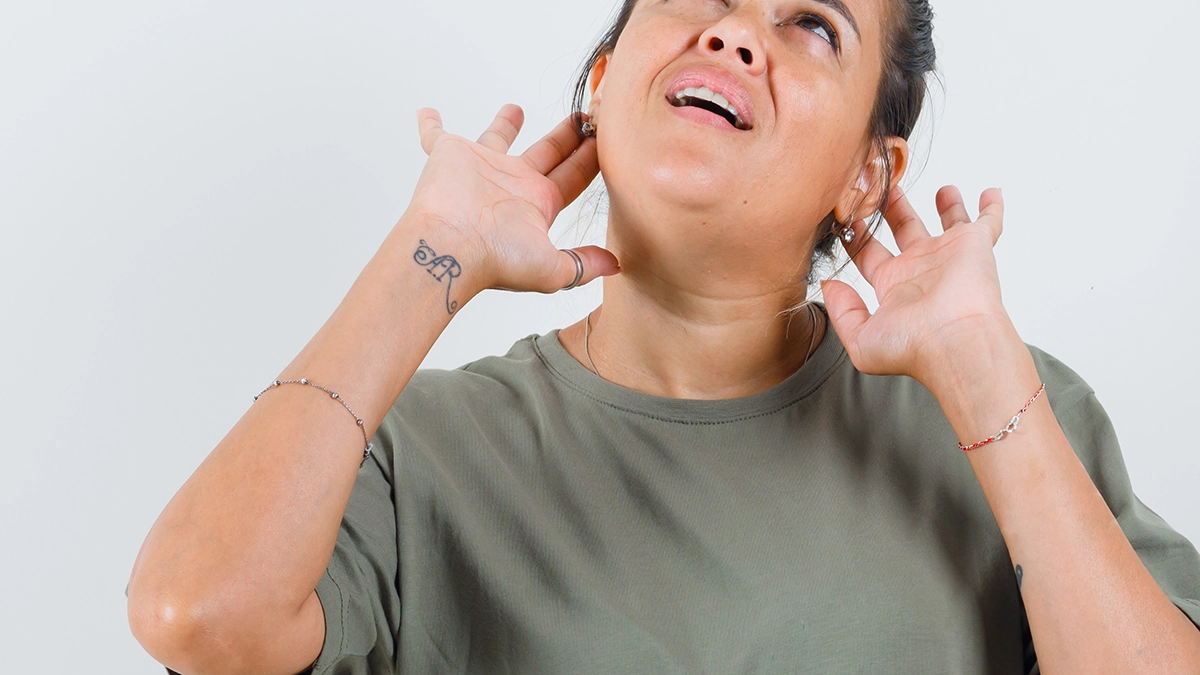 Woman in a green t-shirt holding her fingers to her ears, looking up in discomfort