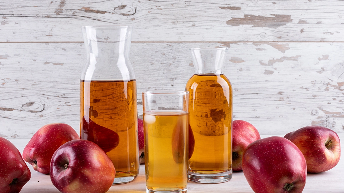 Apple juice in glass carafes with fresh red apples on a rustic table, highlighting natural wellness