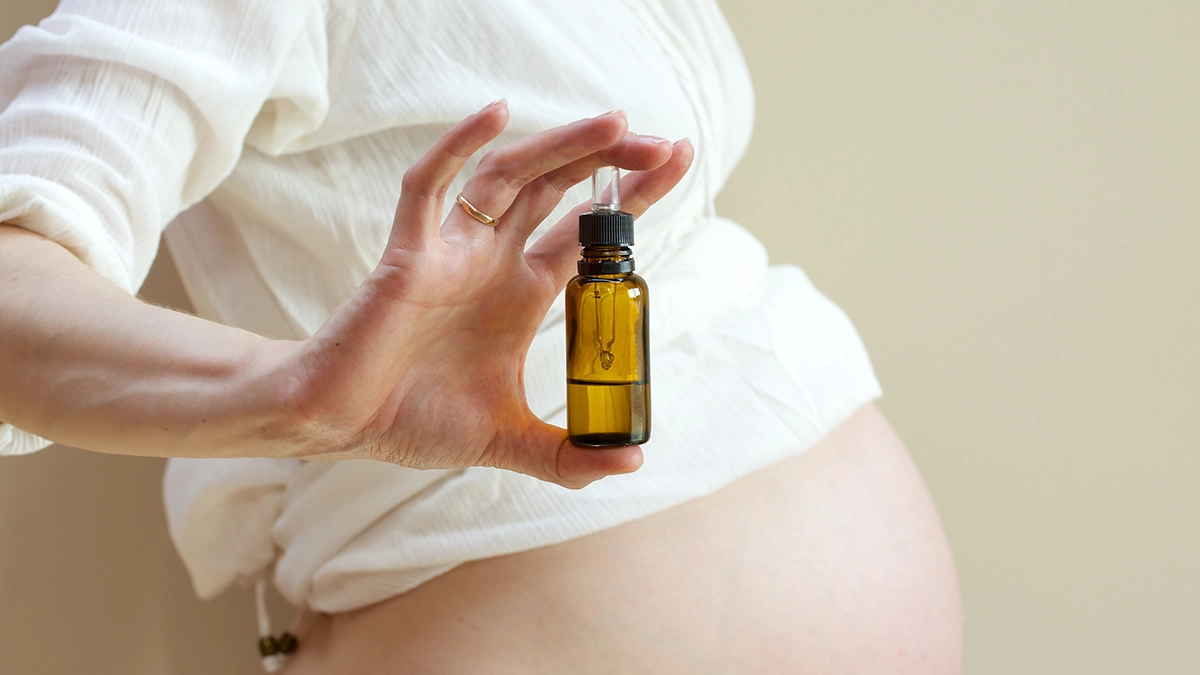 Pregnant woman holding a small amber bottle of essential oil, representing recommendations for using essential oils during labor