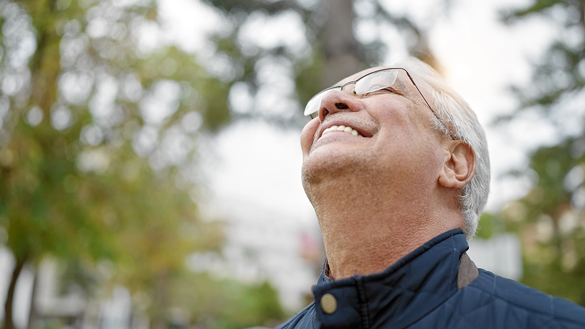 A smiling older man outdoors, looking up, representing olfactory enrichment and its benefits for brain health