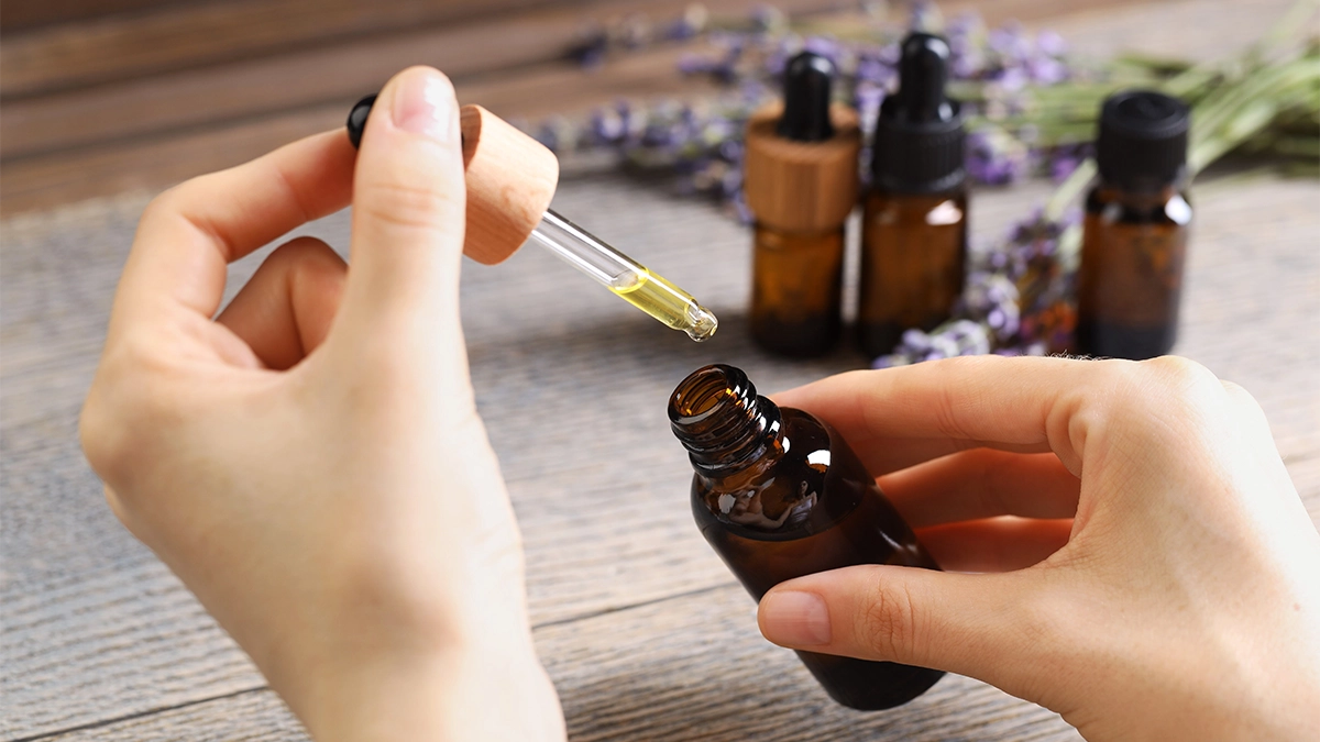 hair, Hands-holding-a-dropper-and-amber-essential-oil-bottle-with-lavender-flowers-and-bottles-in-the-background