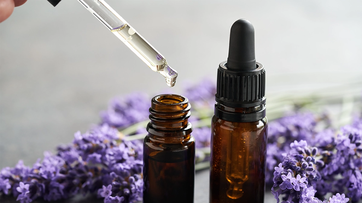 Two amber dropper bottles of lavender essential oil with fresh lavender flowers around them. A dropper is releasing oil into one bottle, illustrating the use of lavender oil, which may have calming benefits but can also cause side effects such as skin irritation, allergic reactions, hormonal effects, headaches, or nausea in sensitive individuals