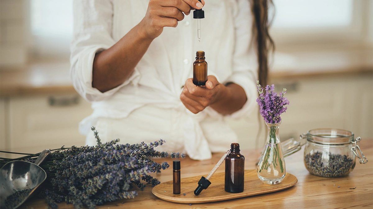 Person handling lavender essential oil with dropper and flowers on a table, illustrating safe use to reduce side effects