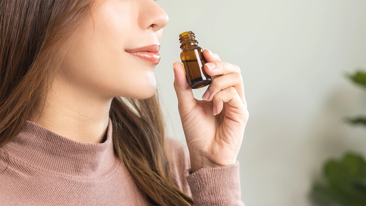 Woman inhaling lavender essential oil from a small amber bottle, illustrating possible inhalation side effects