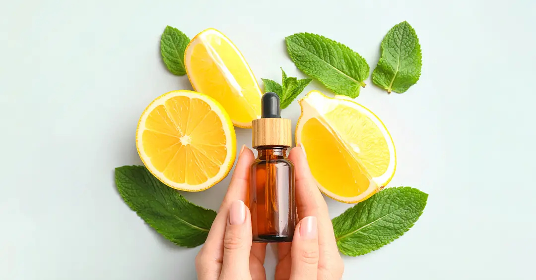 Essential oil bottle held by hands, surrounded by fresh lemon slices and mint leaves.