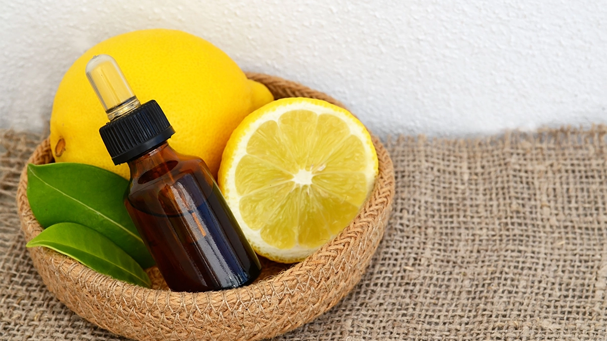 A small amber essential oil bottle placed in a woven basket with fresh lemons and green leaves