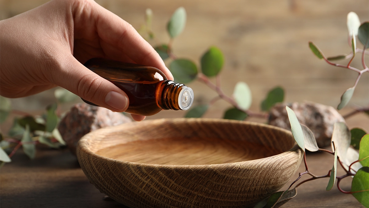 Hand pouring essential oil into a wooden bowl, symbolizing natural ways to energize your morning and start the day right