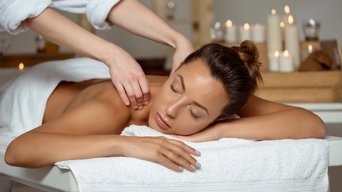 Woman relaxing during an aromatherapy massage at a spa, receiving a shoulder massage with organic aroma oils, surrounded by soft candlelight