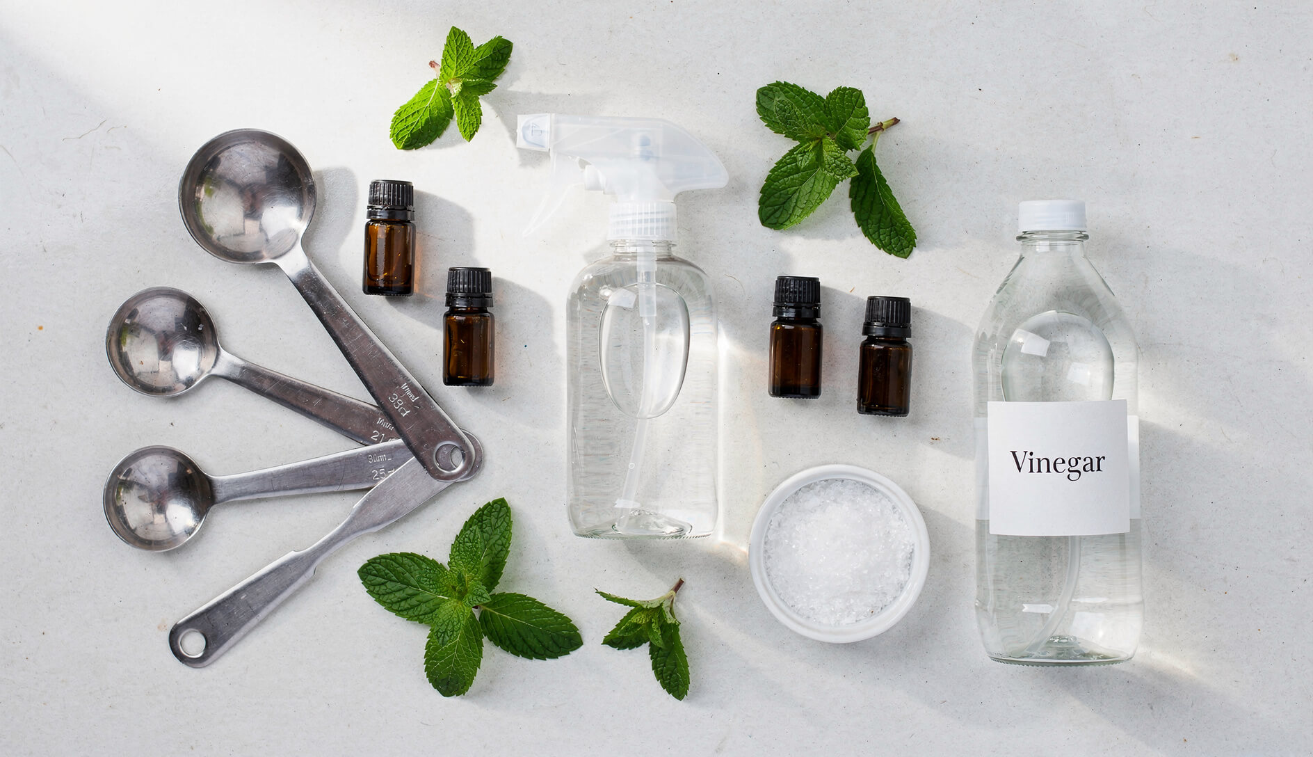 DIY essential oil cockroach repellent spray ingredients on counter with spray bottle and fresh herbs