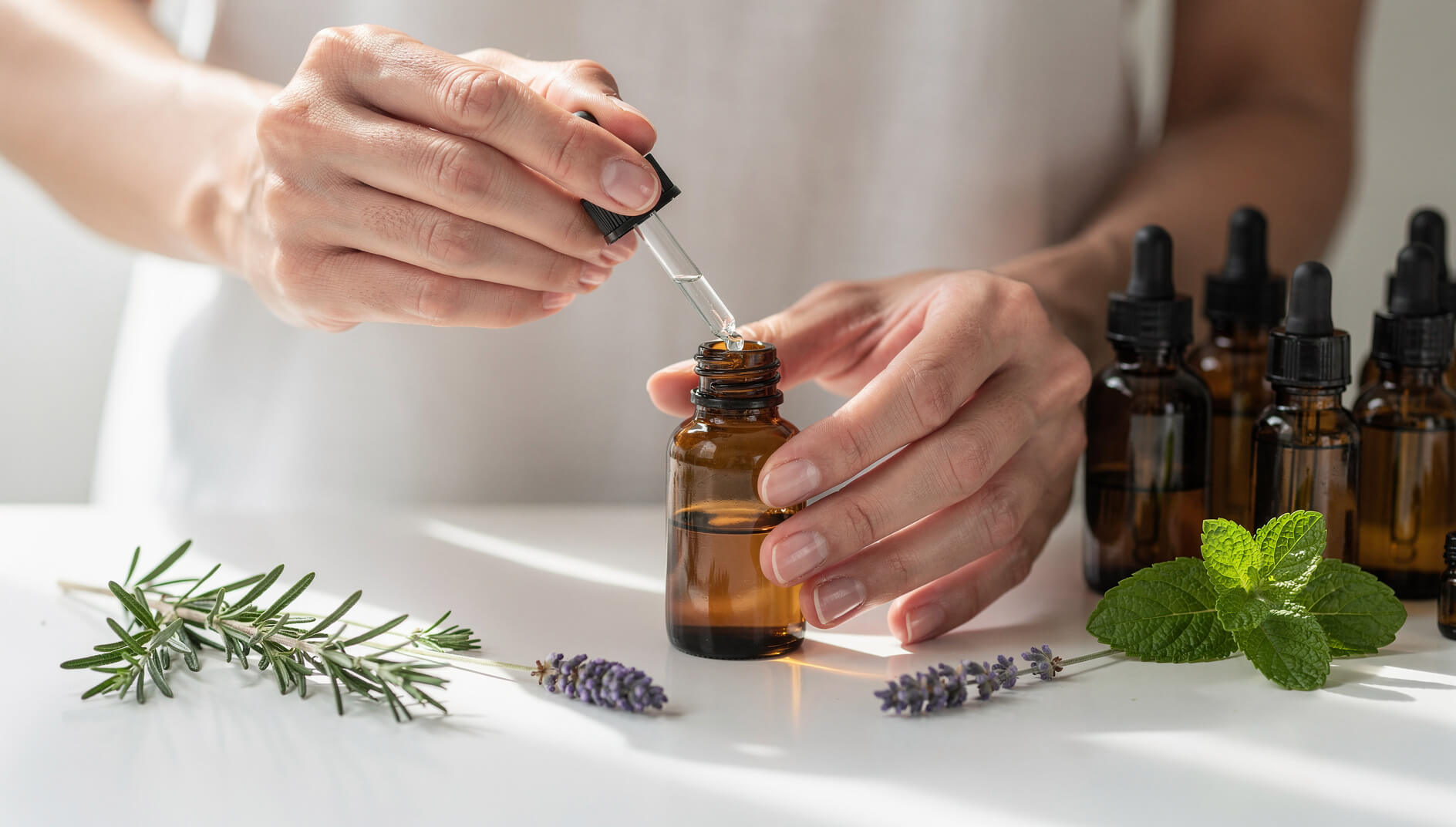 Hands blending aromatherapy essential oils with glass droppers on clean counter