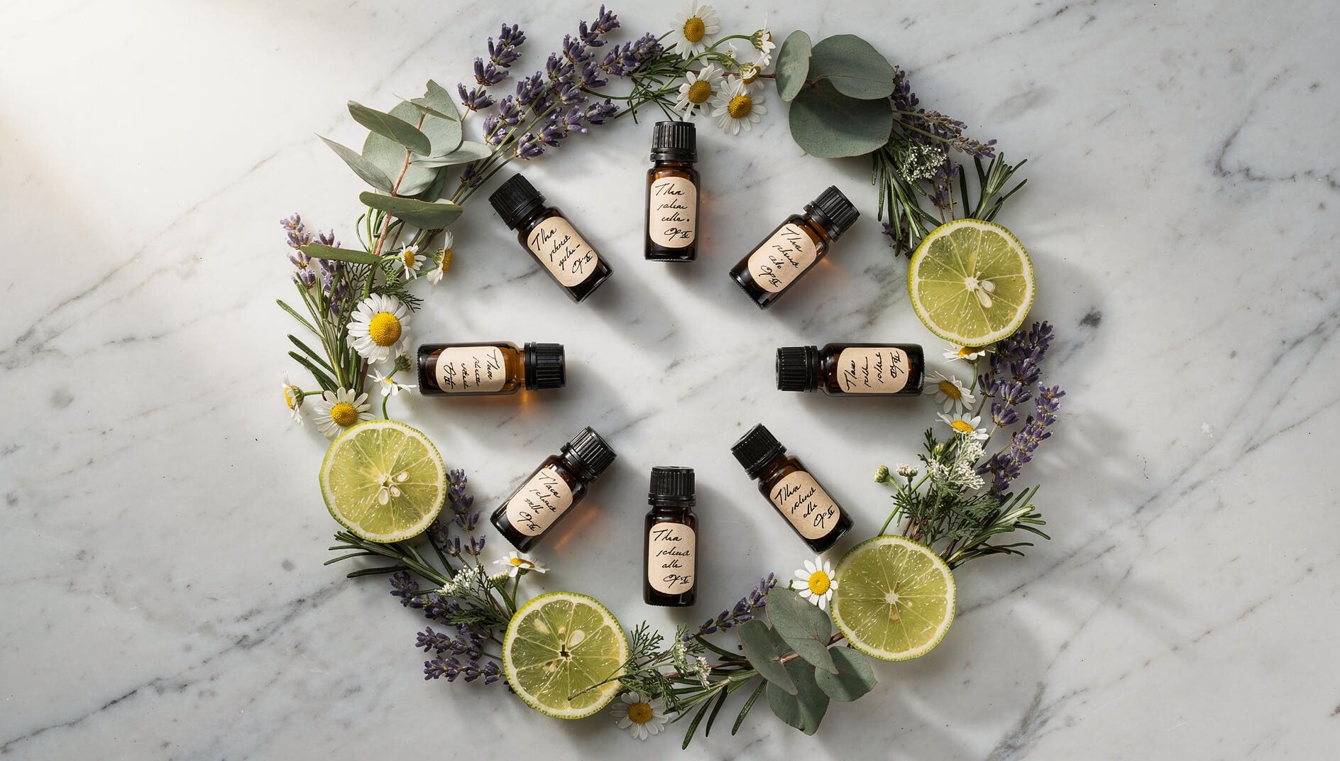 Flat lay of essential oil bottles surrounded by fresh botanicals on white marble