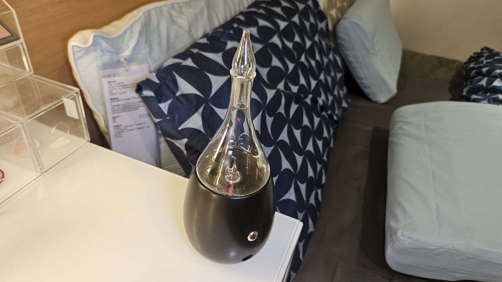 Nebulizing Diffuser on a bedside table next to a bed, demonstrating waterless aromatherapy in a real home setting